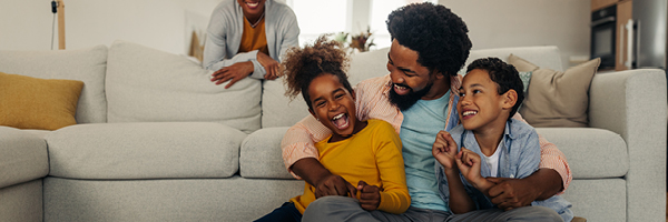 In a living room a smiling woman stands near a laughing man who is embracing two happy children.